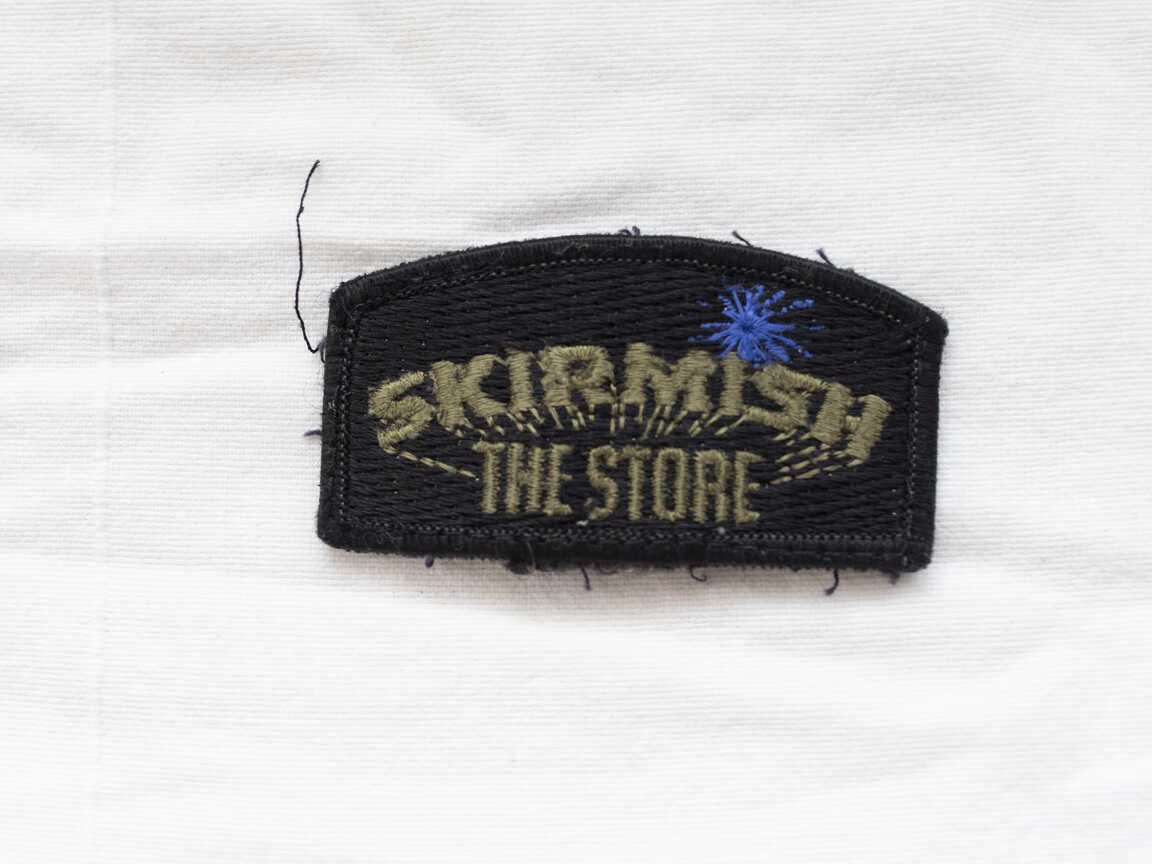 Skirmish Store patch, blue splat, used shape, has stitching and staining on back